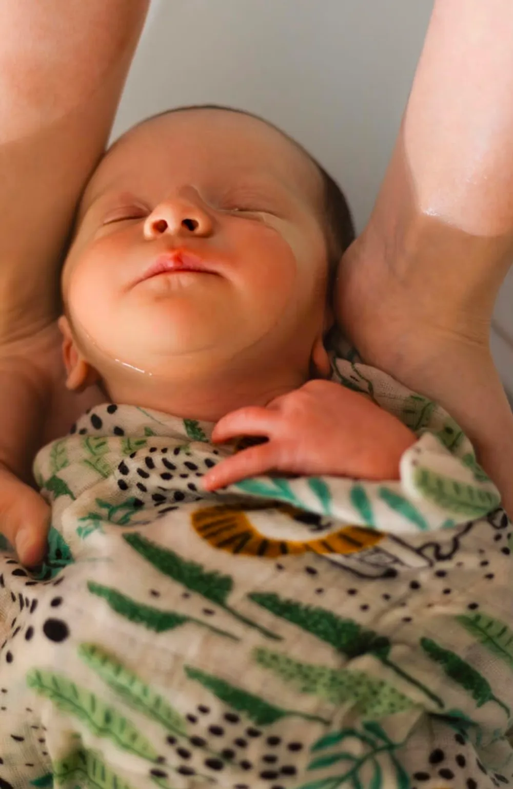 Nuque du bébé soutenue par les mains de la praticienne, lange à motif feuillage
