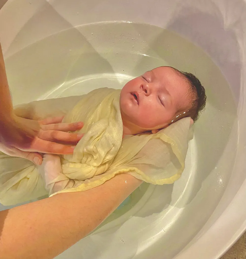 Bébé endormi dans un lange jaune pendant le bain enveloppé