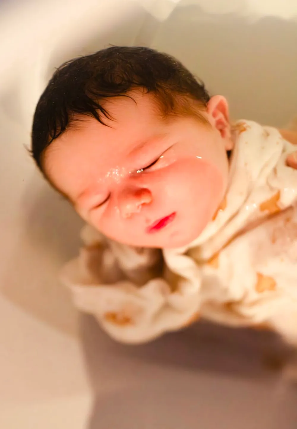 Nouveau-né endormi dans un lange à oursons, bercé dans la baignoire