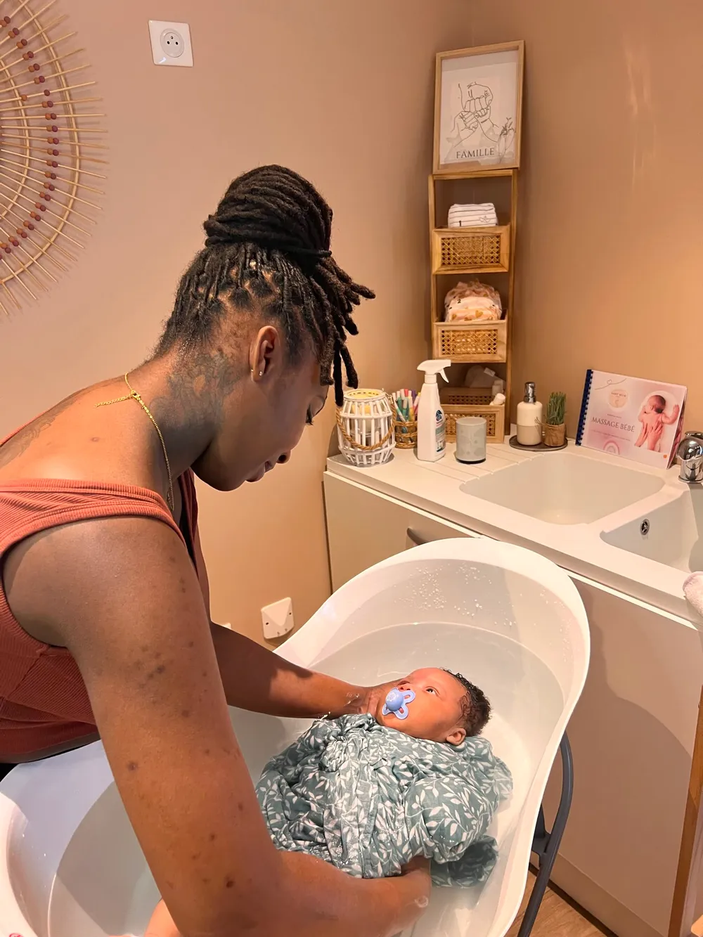 Maman accompagnant son bébé emmailloté dans un lange vert lors du bain enveloppé