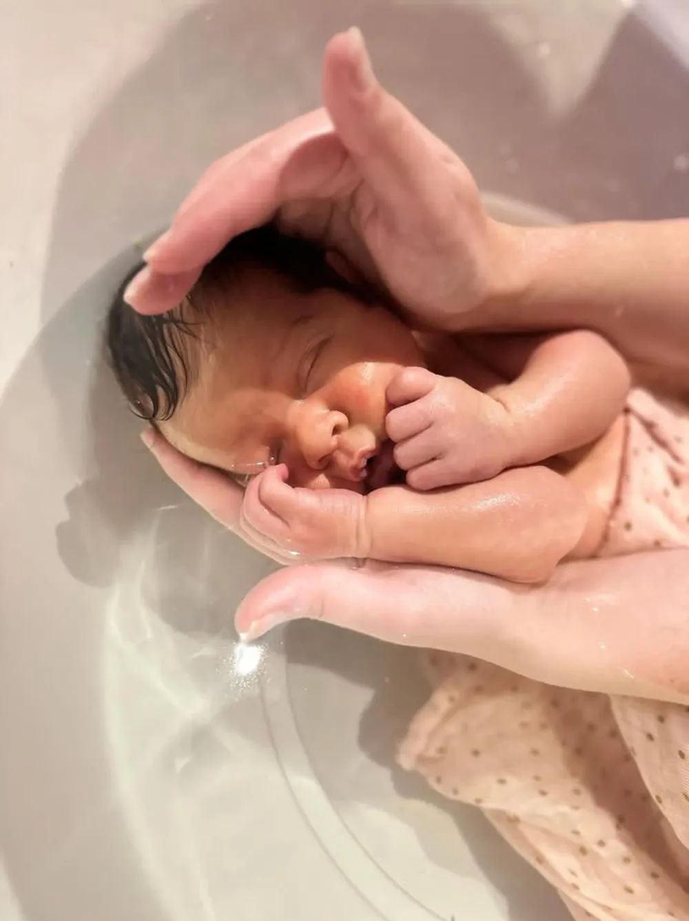Tête du nouveau-né reposant dans les mains en coupe de la praticienne