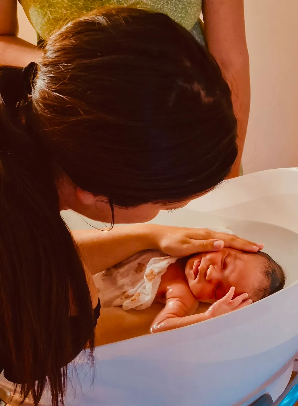 Main de la praticienne posée sur la tête du bébé pendant le bain enveloppé