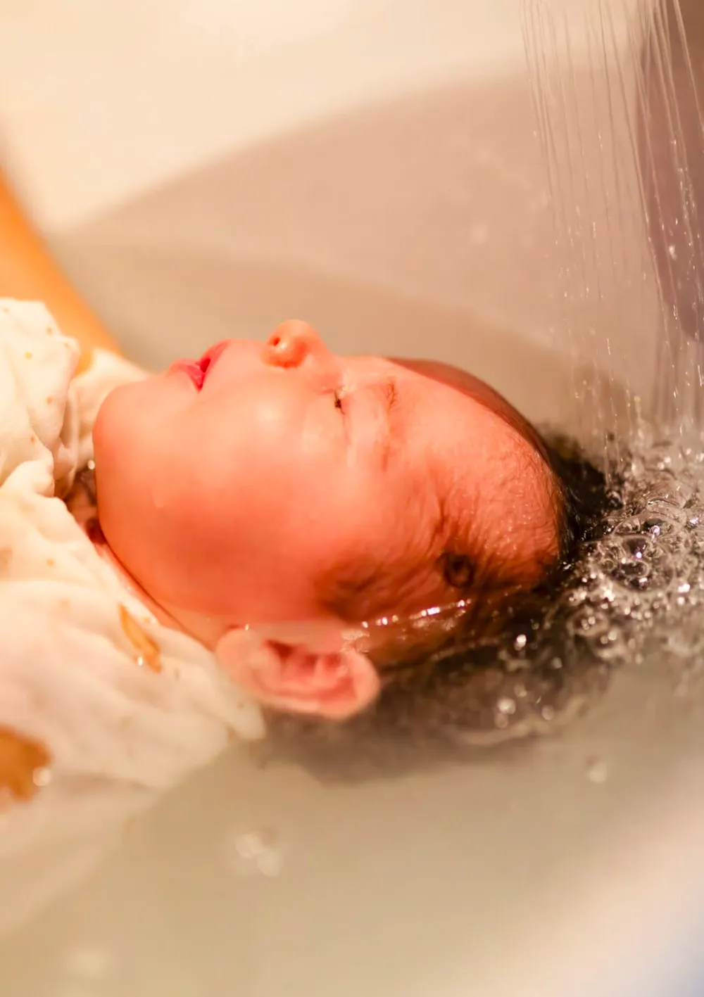 Rinçage tout en douceur des cheveux du bébé pendant le bain enveloppé