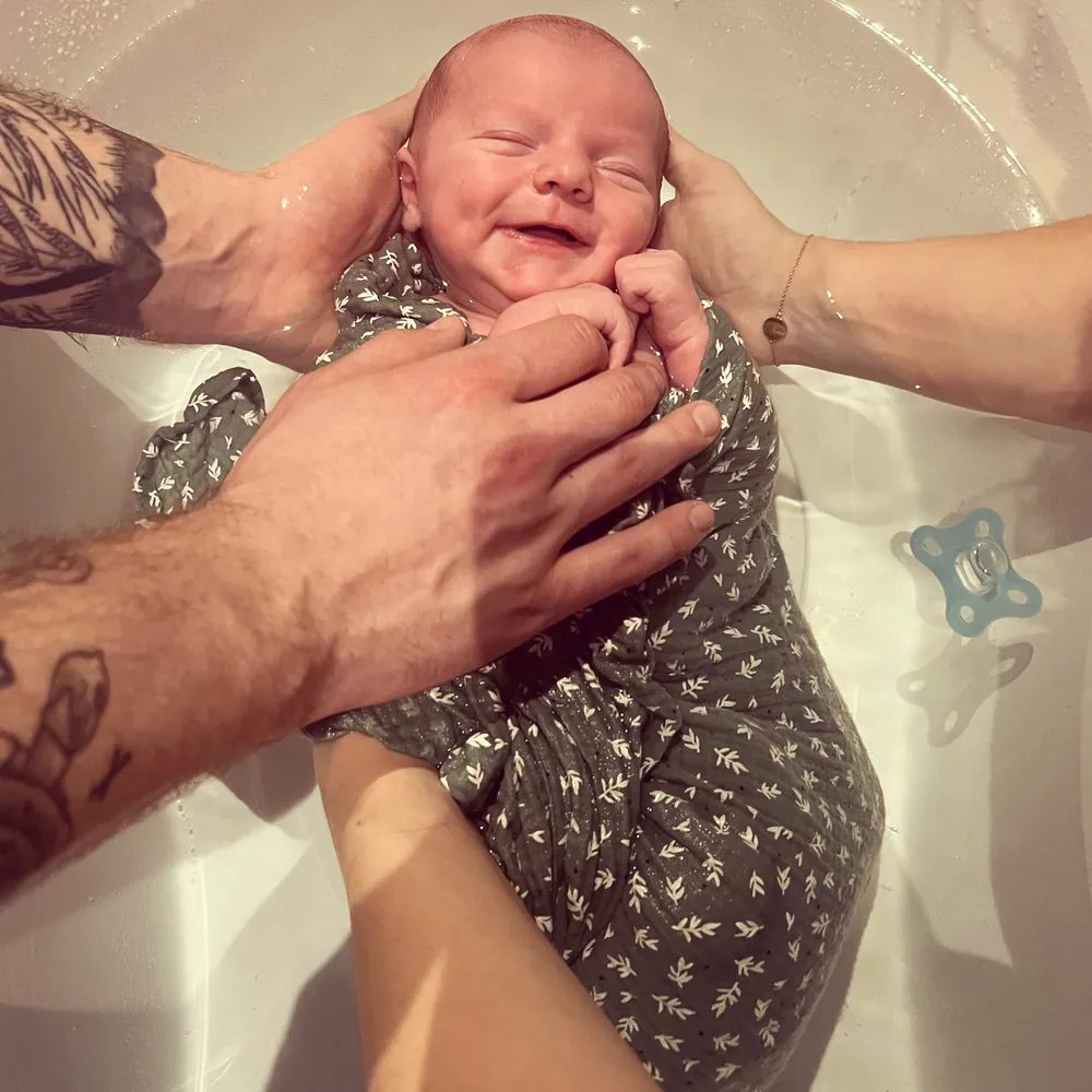 Nouveau-né souriant dans l'eau, entouré des mains de ses deux parents