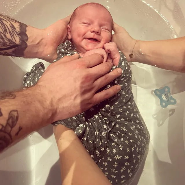 Nouveau-né souriant dans l'eau, entouré des mains de ses deux parents