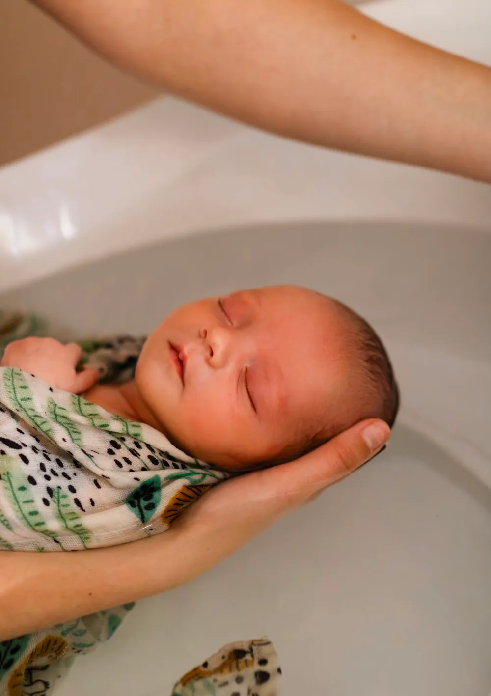 Tête du bébé délicatement soutenue par la main de la praticienne dans l'eau