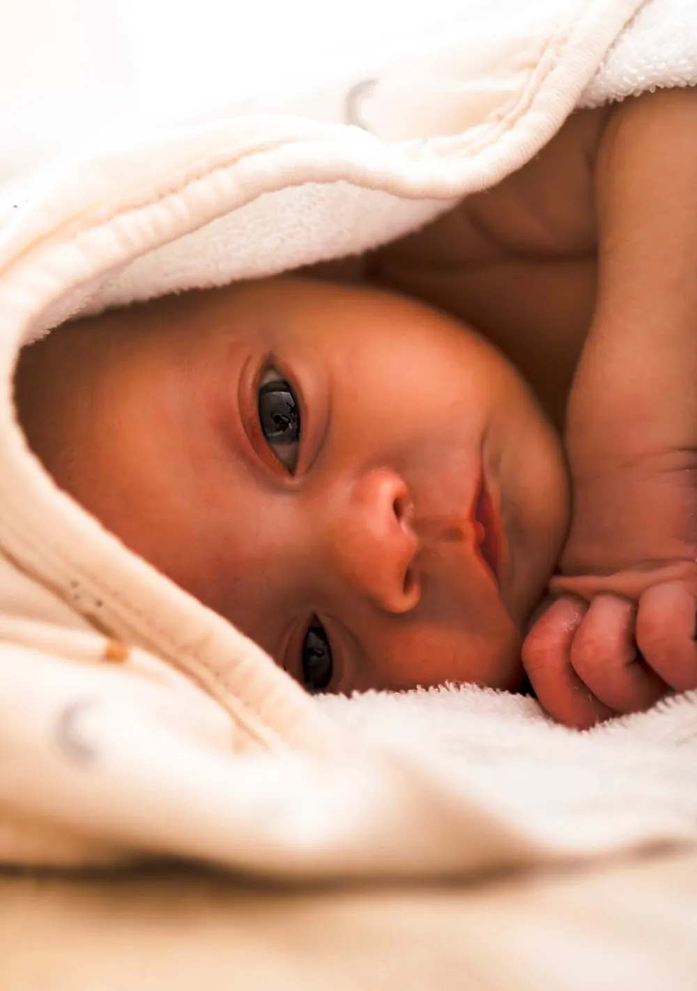 Nouveau-né éveillé et détendu sous sa cape de bain après le bain enveloppé