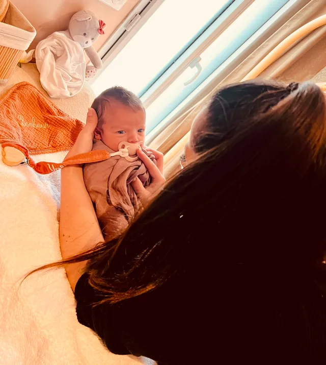 Bébé emmailloté dans les bras de la praticienne près de la fenêtre