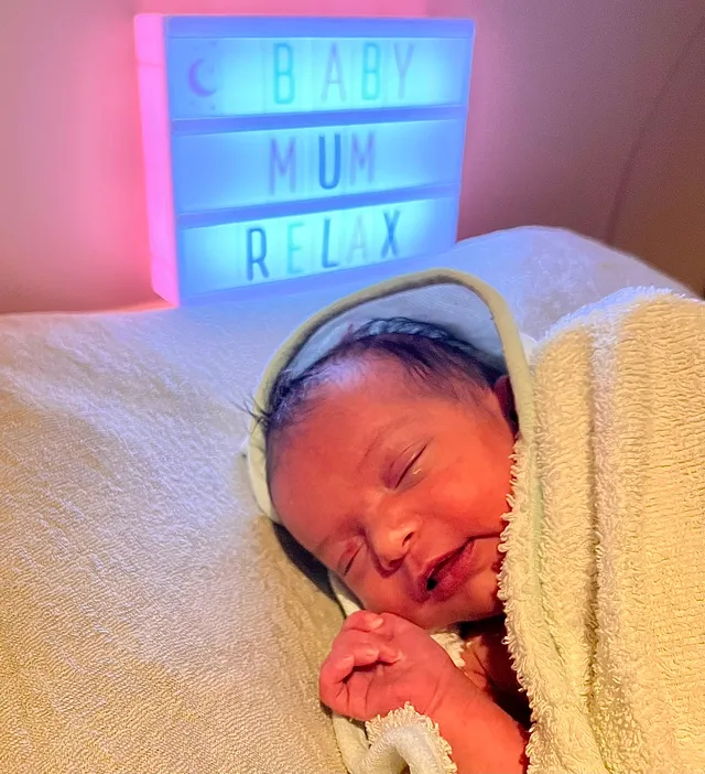 Nouveau-né endormi devant l'enseigne lumineuse BabyMum Relax après son bain enveloppé
