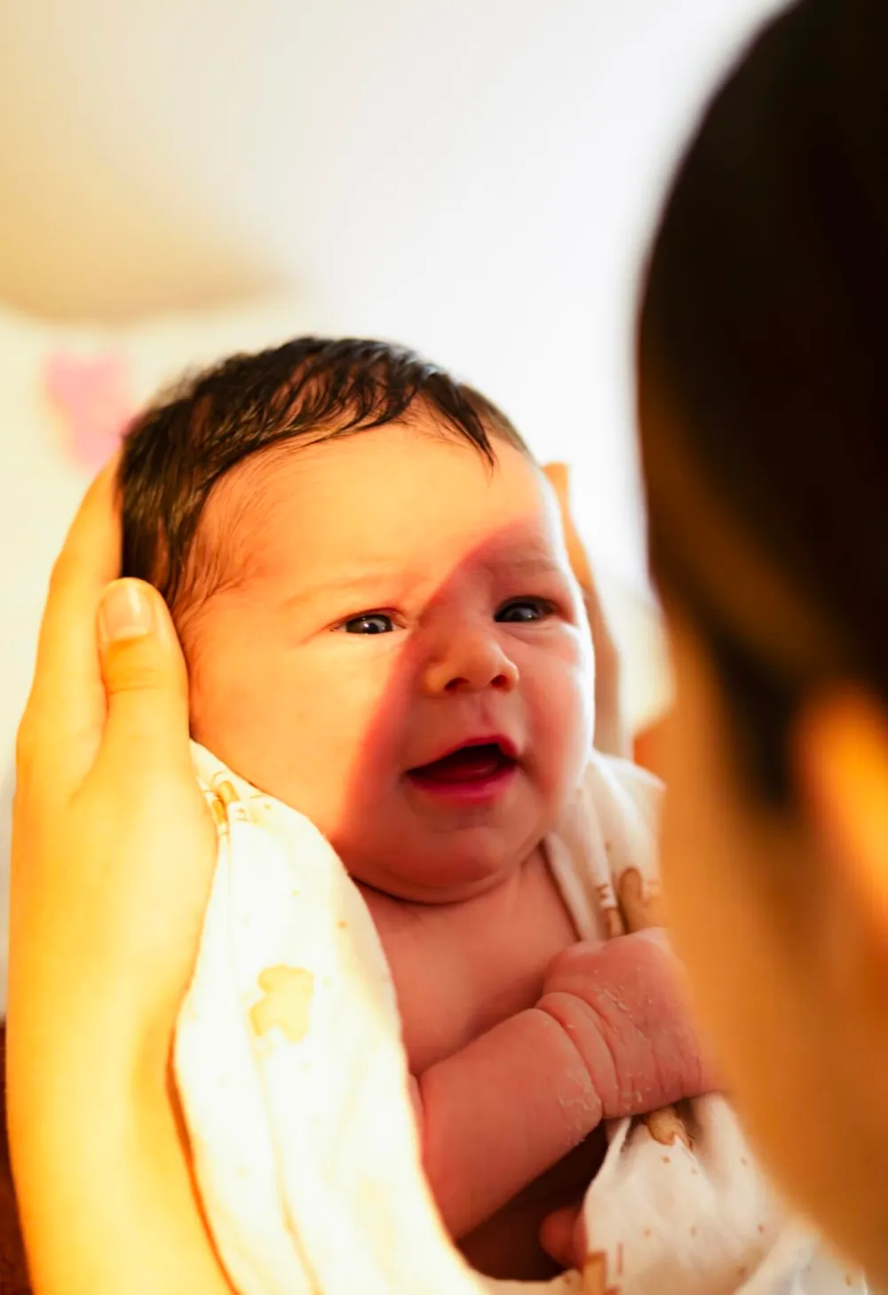 Bébé éveillé enveloppé dans une serviette, tête soutenue après le bain